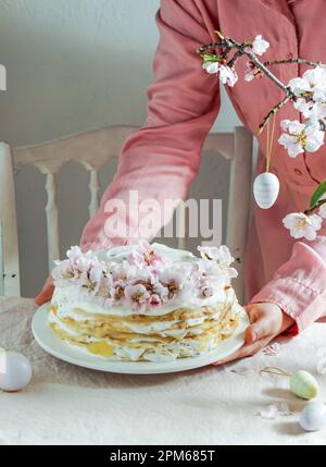 Gâteau de crêpe ou gâteau de blini pour la fête de Pâques, fond rose rose, fleurs d'amande, fond rose rose, mains de femme Banque D'Images