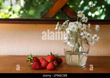 Fraises fraîches et bouquet de belles fleurs blanches de neige en été sur une table en bois. Espace pour le texte Banque D'Images