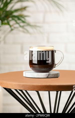 Tasse de café en verre avec élégant dessous de verre en pierre sur table en bois dans la chambre Banque D'Images