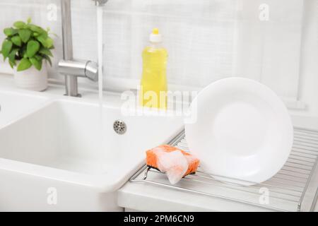 Panier de séchage avec plaque propre et éponge savonneuse dans une cuisine élégante Banque D'Images