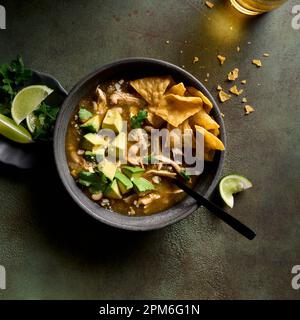Soupe de poulet vert au piment dans un bol garni d'avocat, de coriandre, de tortillas et de cotija. Banque D'Images