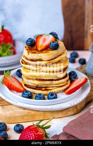 Une pile de crêpes garnies de bleuets et de fraises sur une assiette blanche. Banque D'Images