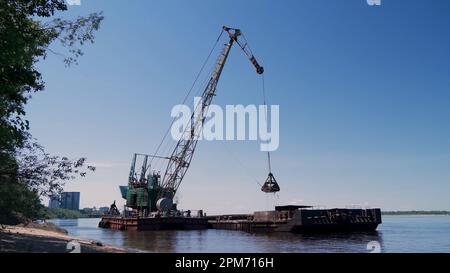 Vue sur une grue flottante déchargeant le sable d'une barge amarrée sur la plage. Préparation pour la saison estivale de la plage. Banque D'Images