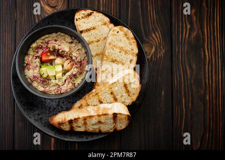 Houmous à l'avocat et aux tomates sur une assiette noire avec toasts de pain, sur fond de bois Banque D'Images