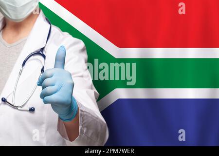 Main du médecin sud-africain montrant le pouce vers le haut geste positif sur le drapeau de fond sud-africain Banque D'Images