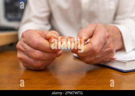Dentiers dans les mains d'un homme dans un manteau blanc. Gros plan. Banque D'Images