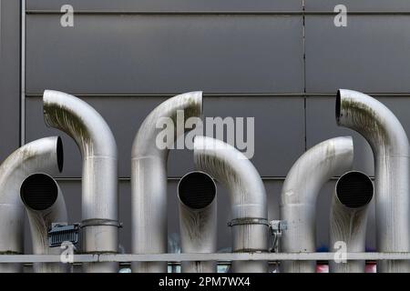 Tuyaux d'échappement métalliques incurvés contre un mur gris. Banque D'Images