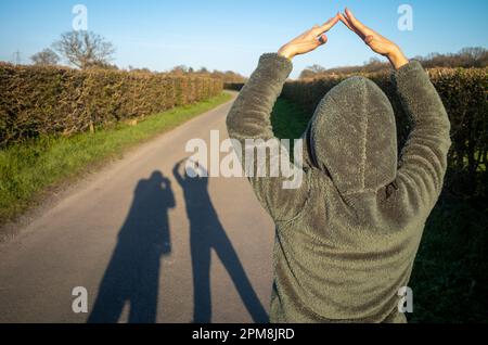 Une femme frappe une pose pour former une ombre allongée d'un couple alors qu'elle se promènait dans la soirée sur une voie de campagne à Billingshurst, West Sussex, Royaume-Uni. Banque D'Images