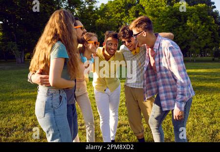 Positifs jeunes hommes et femmes différentes nationalités embrassant et avec le sourire parlant stand dans le parc Banque D'Images