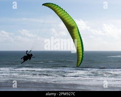 Un parapente vole au-dessus d'un océan faisant un tour à sa droite avec la mer et les vagues en arrière-plan.Backlit silhouette.Sport.Loisirs Banque D'Images