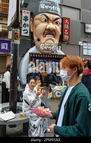 Osaka, Japon - 21 mars 2023 : les gens qui mangent de la nourriture de rue dans le quartier de Dotonbori à Osaka, au Japon. Banque D'Images