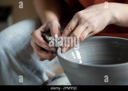 Mains céramiste femelle travaillant avec la roue de potier tournant pour niveler les murs de la cuve d'argile de gros plan Banque D'Images