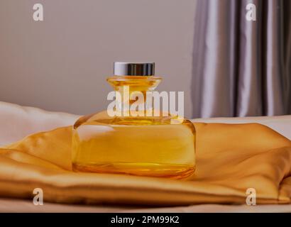 Bouteille de parfum reposant sur un tissu de soie avec la lumière de fenêtre le frappant. Banque D'Images