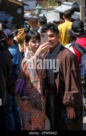 Kyoto, Japon - 28 mars 2023: Un couple vêtu de kimonos prendre un selfie sur Sannenzaka, une rue piétonne pavée à Kyoto, Japon. Banque D'Images