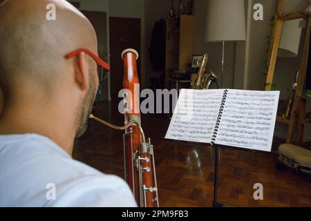 vue arrière, chauve-personne non reconnaissable vêtu de blanc assis à la maison étudiant la musique classique avec son basson. Banque D'Images