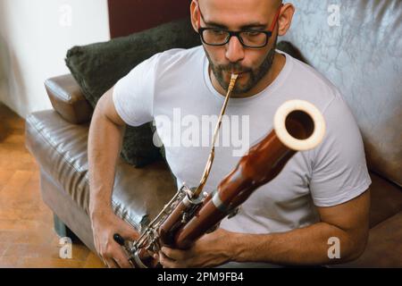 vue de face de latino homme d'origine vénézuélienne, avec barbe, tête chauve et lunettes, assis sur le canapé dans la salle de séjour de la maison concentrée Banque D'Images