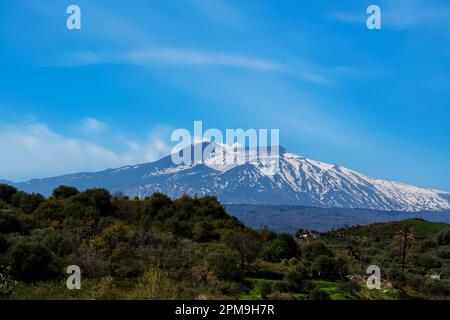 Plan en grand angle de l'Etna recouvert de neige, qui fait éclater des bouffées de vapeur blanches contre un ciel bleu intense Banque D'Images