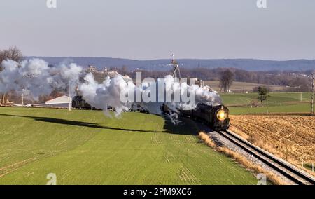 Une locomotive à vapeur d'époque voyageant le long d'un ensemble de voies de chemin de fer coupant à travers une prairie verte luxuriante Banque D'Images