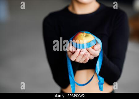 Concept de régime. Une pomme rouge enveloppée dans un ruban de mesure bleu, une fille tient une pomme dans ses mains. Banque D'Images