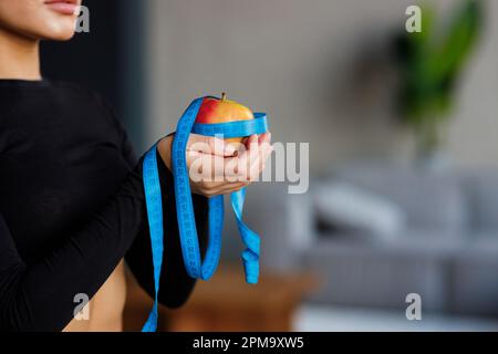 Concept de régime. Une pomme rouge enveloppée dans un ruban de mesure bleu, une fille tient une pomme dans ses mains. Banque D'Images
