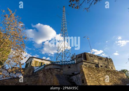Un grand poteau de transmission s’élève au-dessus du rempart vénitien sur le côté grec de la frontière du centre-ville de Nicosie, Chypre. Des tonneaux peints en bleu et blanc surmontent la balustrade, et une petite maison aux volets verts s’appuie contre l’intérieur de la fortification historique. Banque D'Images