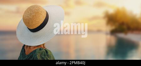 femme méconnaissable avec chapeau de paille regardant le coucher du soleil sur la plage tropicale du complexe. bannière avec espace de copie Banque D'Images