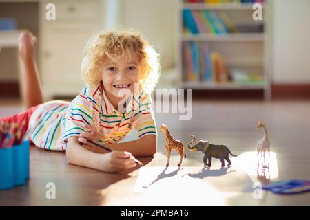 Enfant ombre dessin animaux. Les enfants jouent à la maison. Artisanat amusant pour enfants de maternelle. Un petit garçon peint une girafe et un éléphant dans une chambre ensoleillée. Banque D'Images