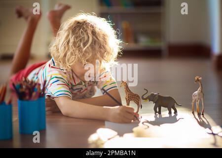 Enfant ombre dessin animaux. Les enfants jouent à la maison. Artisanat amusant pour enfants de maternelle. Un petit garçon peint une girafe et un éléphant dans une chambre ensoleillée. Banque D'Images