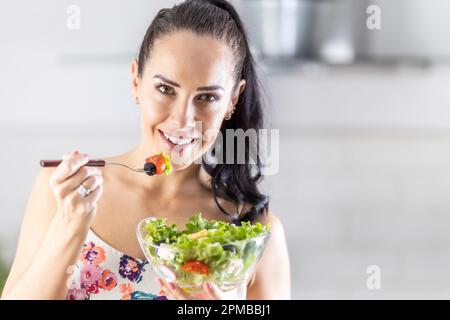 Mode de vie sain jeune femme mangeant de la salade de laitue. Jeune brunette mangeant de la nourriture saine dans sa cuisine. Banque D'Images