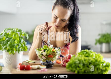 Mode de vie sain jeune femme mangeant de la salade de laitue. Jeune brunette mangeant de la nourriture saine dans sa cuisine. Banque D'Images