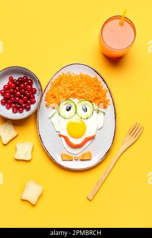 Assiette avec petit déjeuner amusant en forme de clown, baies et verre de jus sur fond orange Banque D'Images