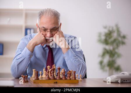 Un vieil employé de sexe masculin joue aux échecs dans le bureau Banque D'Images