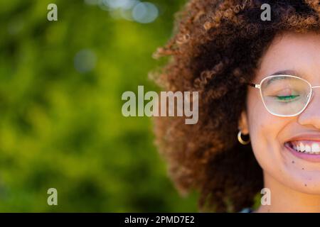 Petit visage de jeune femme biracial avec les yeux fermés et les cheveux afro souriant dans la cour Banque D'Images