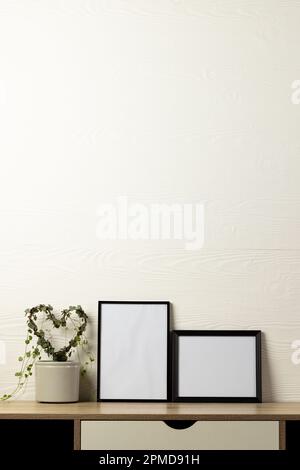Verticale de deux cadres noirs vides avec espace de copie et plante sur la table contre un mur blanc Banque D'Images