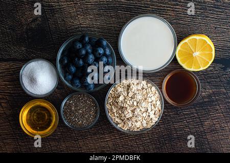 Flocons d'avoine au myrtille et au Chia Ingrédients sur une table en bois : avoine à l'ancienne, myrtilles fraîches, miel et autres ingrédients Banque D'Images