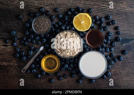 Flocons d'avoine au myrtille et au Chia Ingrédients sur une table en bois : avoine à l'ancienne, myrtilles fraîches, miel et autres ingrédients Banque D'Images