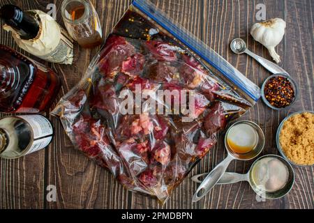 Faire mariner des bouts de steak crus dans un sac de Ziplock en plastique : bouts de boeuf non cuits dans un sac en plastique entouré d'ingrédients de marinade Banque D'Images