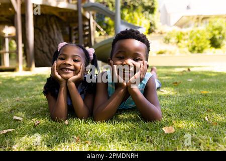Portrait de frères et sœurs afro-américains mignons avec des mains sur des chins allongé sur un terrain herbeux dans le parc Banque D'Images