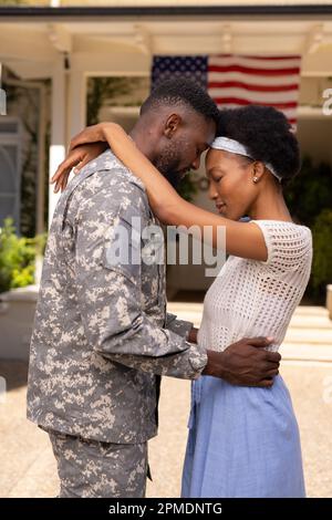 Vue latérale du mari et de la femme d'un soldat afro-américain affectueux avec la tête à la tête à l'extérieur de la maison Banque D'Images