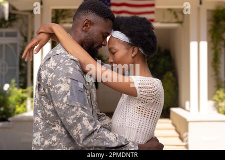 Vue latérale du mari et de la femme soldat de l'armée afro-américaine, de la tête à la tête, debout à l'extérieur de la maison Banque D'Images