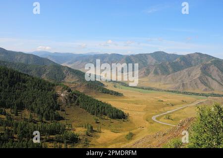 Une route asphaltée étroite traverse une vallée coincée dans les montagnes par une belle journée d'été. Col de Chike-Taman, Altaï, Sibérie, Russie. Banque D'Images