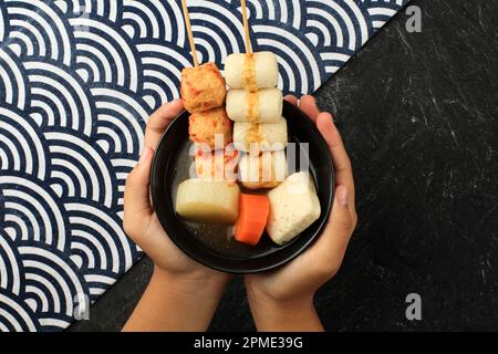 Un bol de brochette à soupe japonaise de boules de poisson Oden, tenue à la main féminine, vue de dessus Banque D'Images