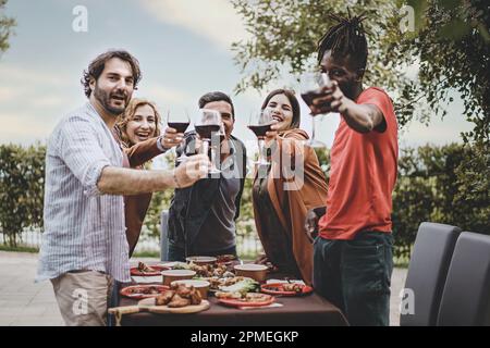 Un groupe d'amis, dont deux hommes et une femme dans leur 40s, une jeune personne de plus de taille, et une personne africaine de 25 ans, debout et avec qui on fait du toaster Banque D'Images