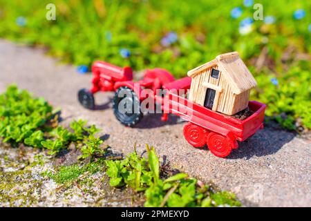 Petite cabine en bois dans la remorque d'un tracteur jouet, placée dans un beau jardin par beau temps ensoleillé. Concept de livraison de cabine de jardin. Banque D'Images