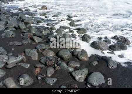 Puissant lavage de vagues au-dessus des roches volcaniques sur la côte d'Hawaï. Banque D'Images