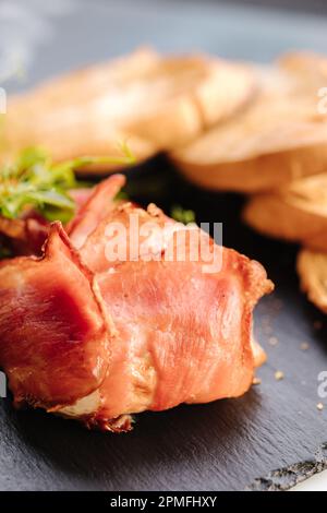 Fromage Camembert cuit au bacon. Morceaux croustillants de baguette et tranches de piment sur un panneau en pierre noire Banque D'Images