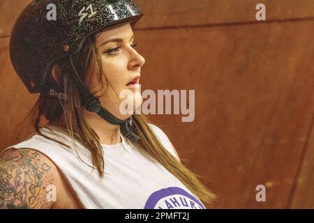 Femme roller derby patineuse avec l'épaule tatouée peut-être debout dans la boîte de pénalité à une ligue mixte scrimmage. Banque D'Images