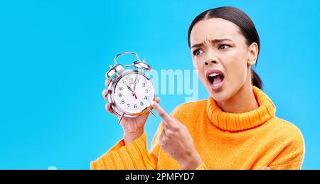 Frustré, le temps et la femme avec un réveil, tard et en colère contre un fond bleu de studio. Femme, criant et personne pointant pour regarder Banque D'Images