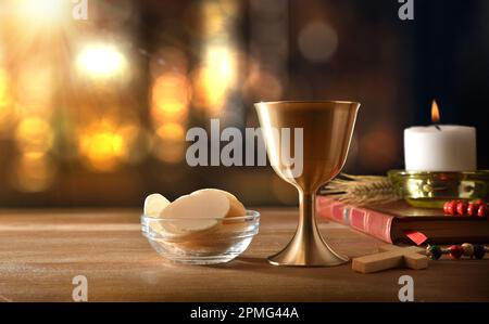 Tasse de vin et hôtes sur table en bois avec bible et bougie pour eucharistie avec rétro-éclairage. Vue avant. Banque D'Images