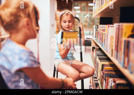 Écolières à la recherche de livres audio dans la bibliothèque de l'école. Étudiants choisissant des livres. L'éducation élémentaire. Faire des devoirs. Apprendre à partir de livres. Retour à sch Banque D'Images